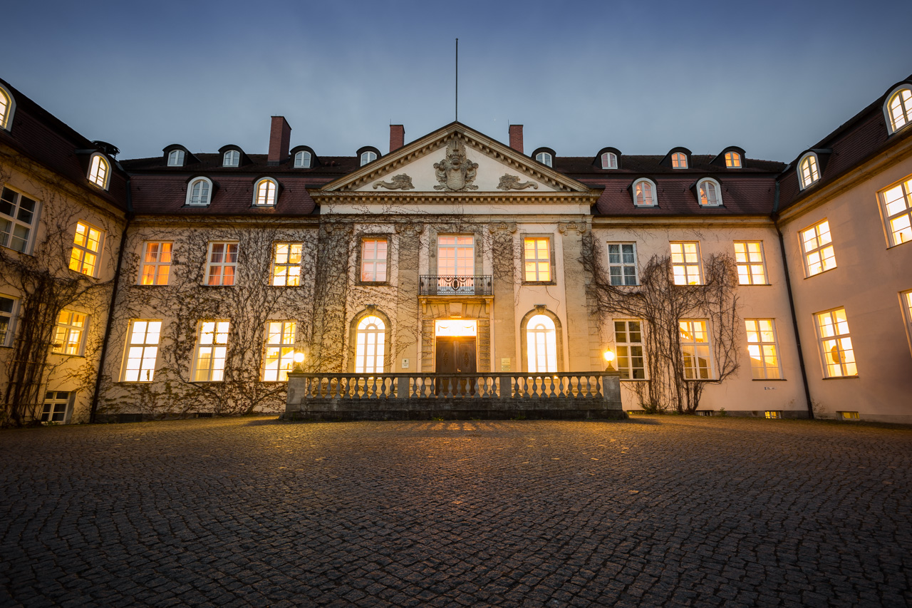 Eingangsfassade des Hotel Schloss Storkau am Abend mit Wappengiebel, Balustrade und gepflastertem Innenhof