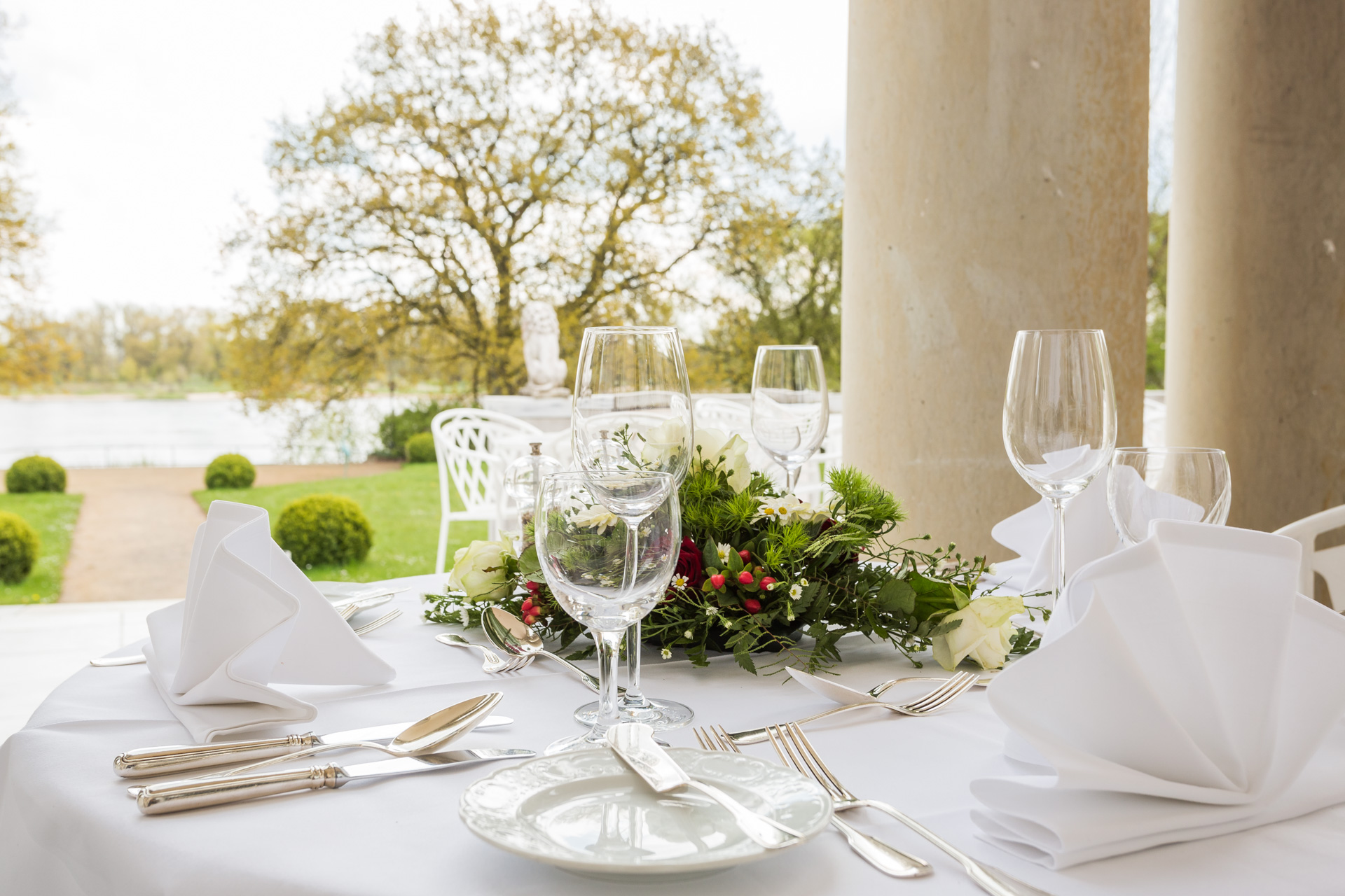 Gedeckter Tisch mit Blumengesteck unter den Säulen der Elbterrasse des Hotel Schloss Storkau mit Blick auf die Elbe