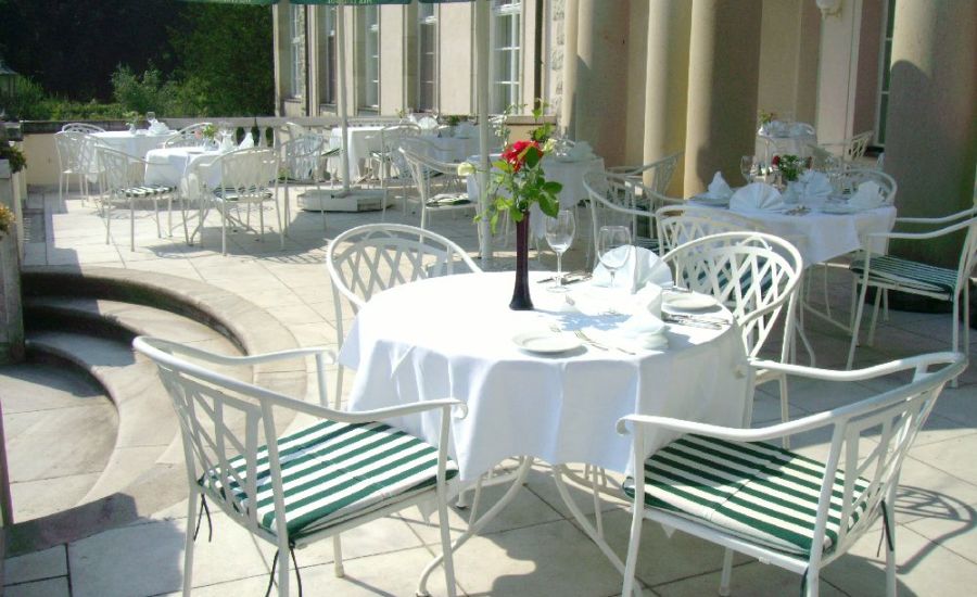 Elbterrasse des Hotel Schloss Storkau mit mehreren gedeckten Tischen und weißen Gartenstühlen mit grün-weiß gestreiften Kissen