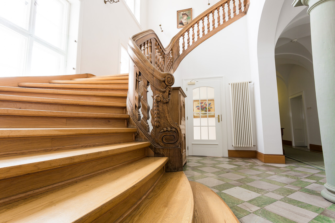 Historische Holztreppe im Treppenhaus des Hotel Schloss Storkau mit geschnitztem Geländer und grün-weiß kariertem Steinboden