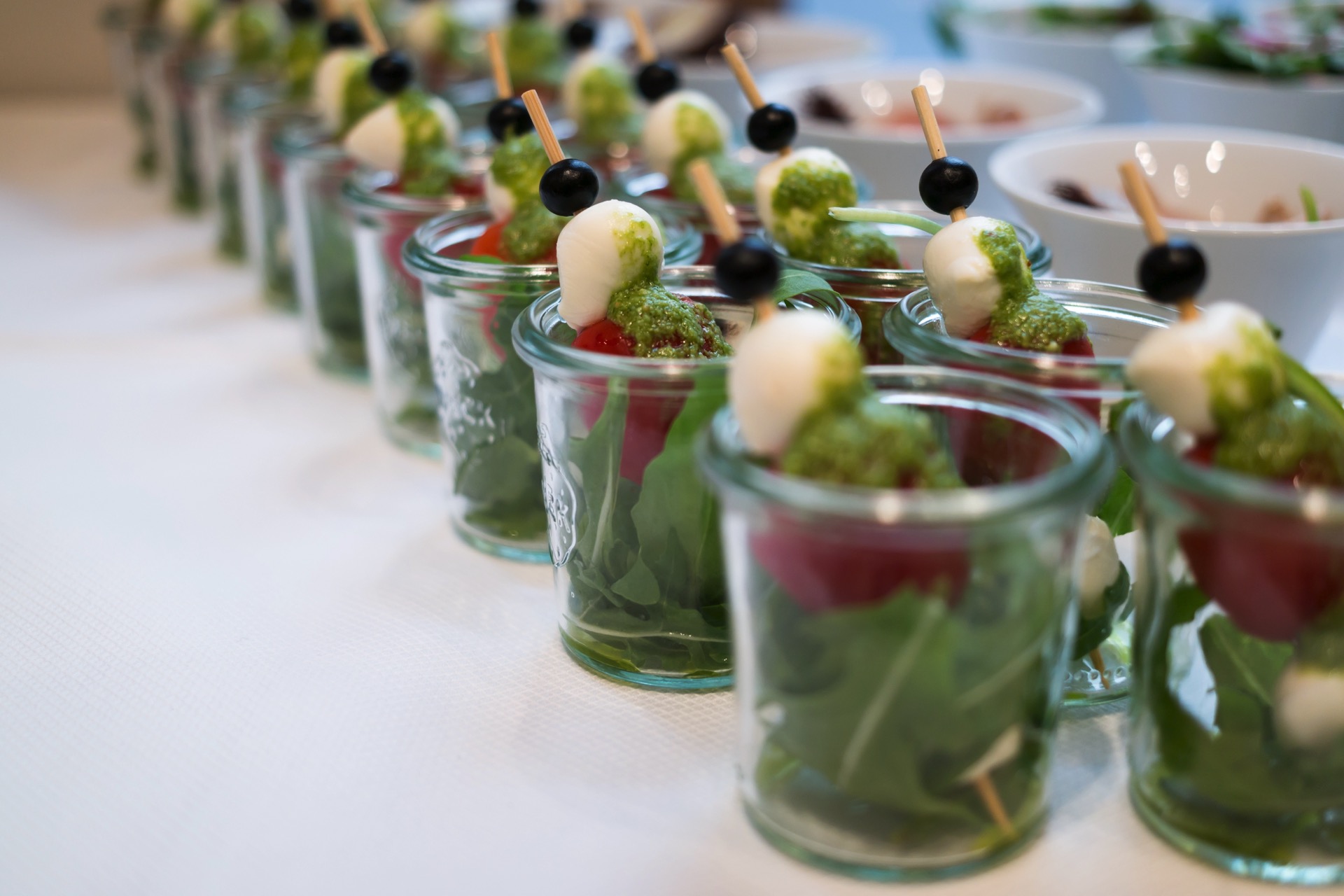 Reihe von Caprese-Vorspeisen im Glas mit Rucola, Tomate, Mozzarella, Pesto und Olive am Spieß