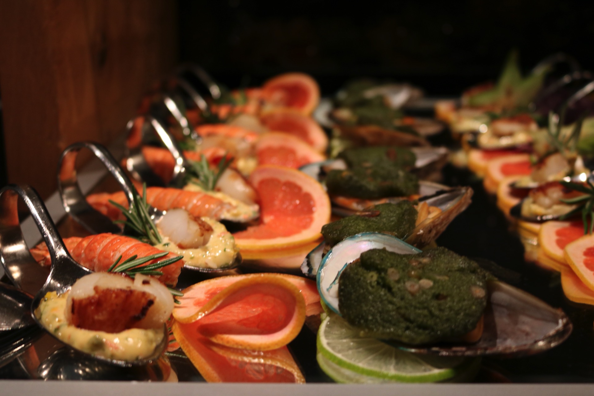 Meeresfrüchte-Löffel auf einem Buffet mit Garnelen, Jakobsmuscheln, Miesmuscheln, Pesto und Grapefruit
