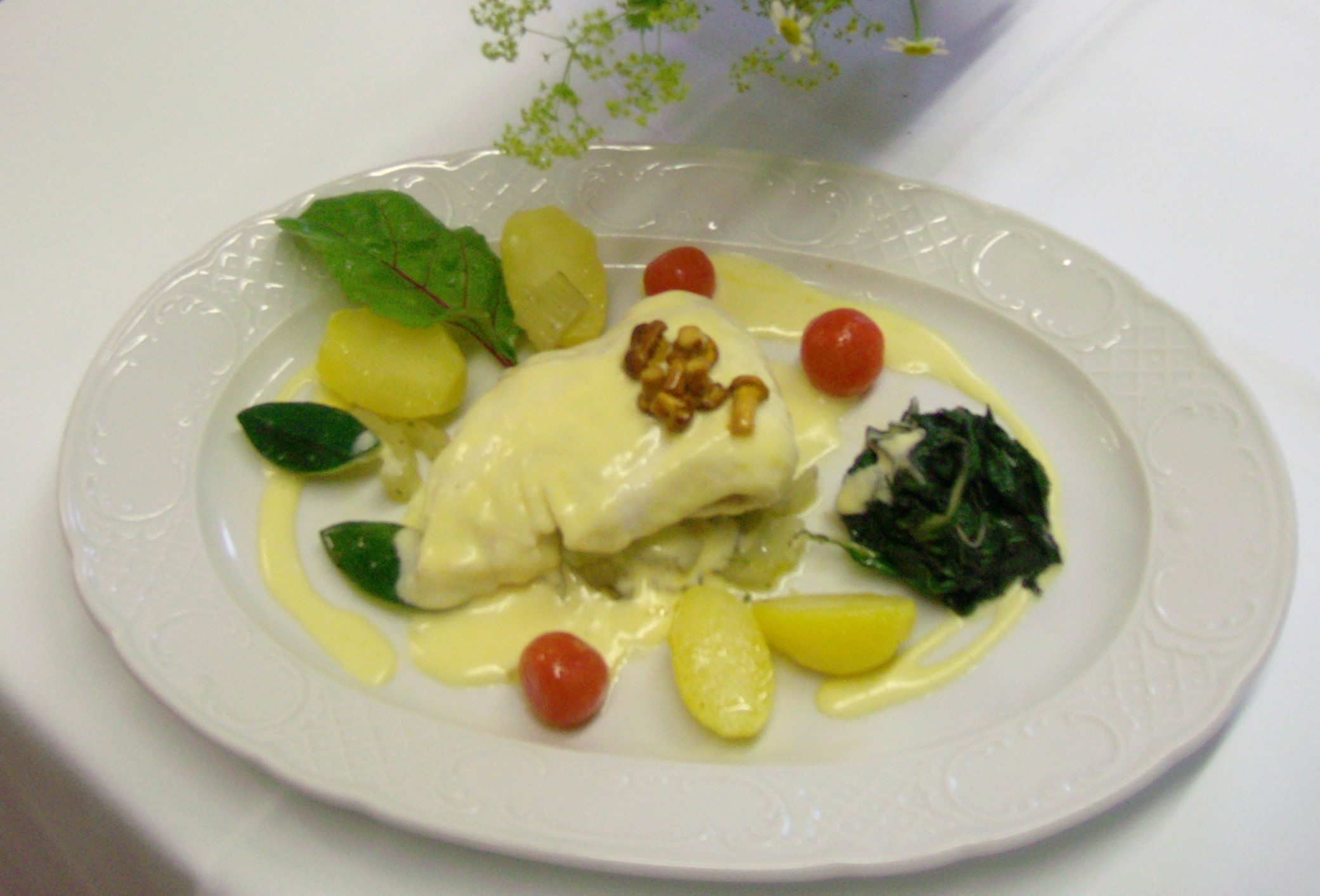 Pochiertes Fischfilet mit heller Sauce, Walnüssen, Blattspinat und Kartoffeln auf weißem Teller im Hotel Schloss Storkau
