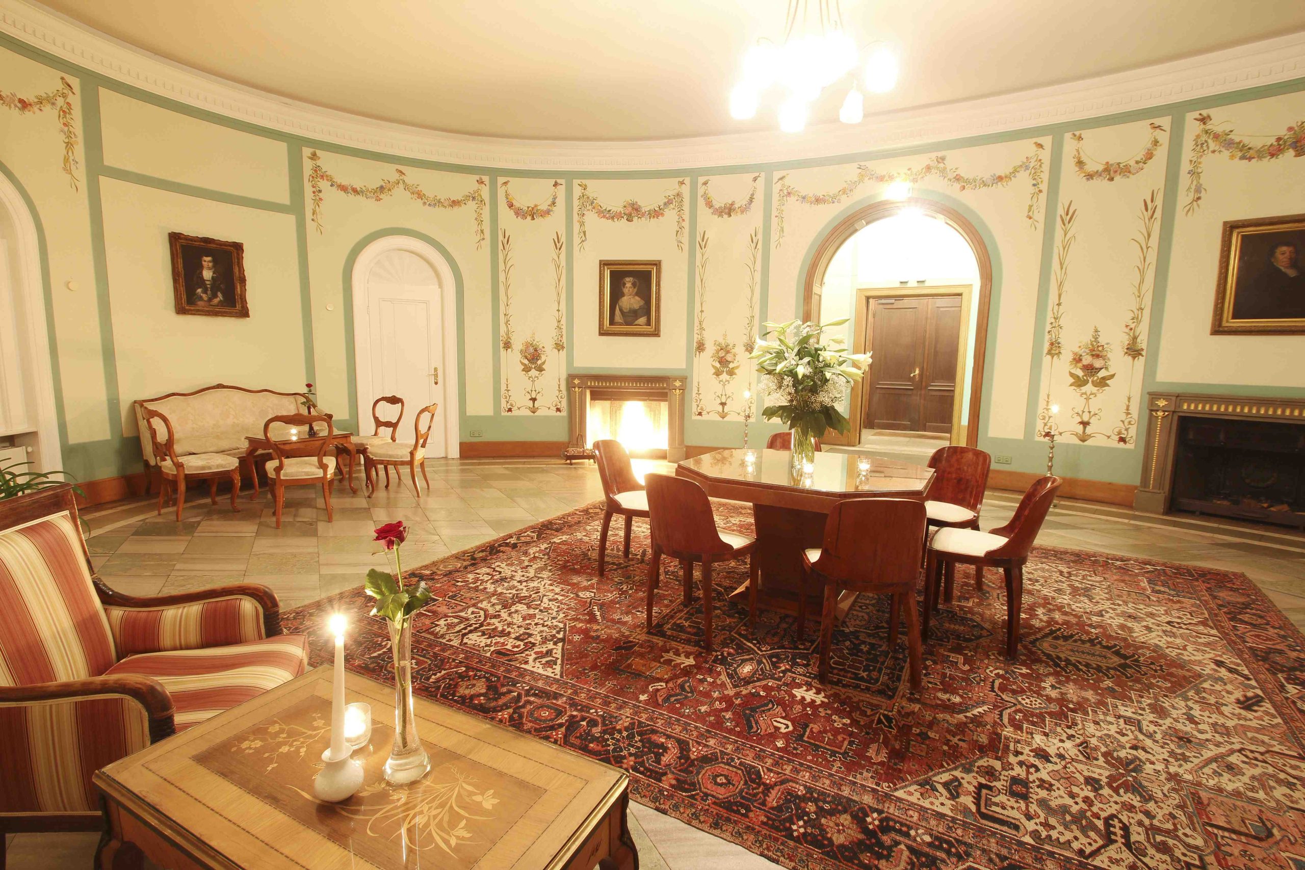 Ovaler Salon im Hotel Schloss Storkau mit achteckigem Tisch, sechs Stühlen, Lilienstrauß und zwei Kaminen