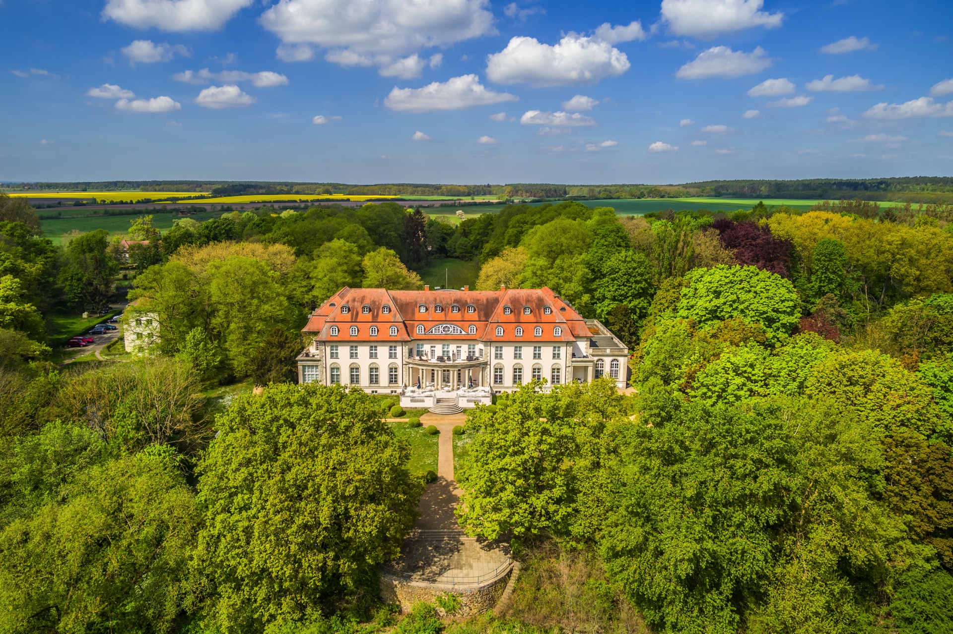 Luftaufnahme der Parkseite des Hotel Schloss Storkau mit Terrasse, Säulenvorbau und Wegeachse durch den grünen Schlosspark