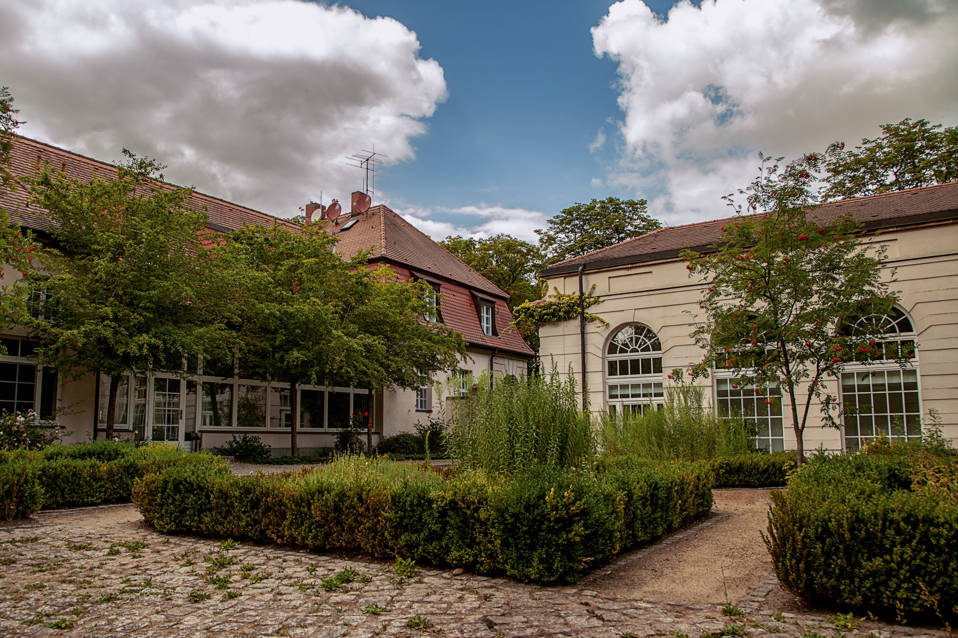 Innenhof am Palmenhaus des Hotel Schloss Storkau mit Buchsbaumhecken, gepflastertem Weg und hohen Sprossenbogenfenstern des Tagungsgebäudes