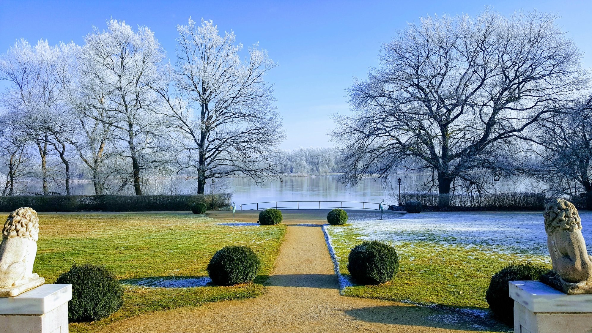 Winterlicher Schlosspark des Hotel Schloss Storkau mit Löwenskulpturen, Buchskugeln und Weg zum Ufer der Elbe bei Raureif