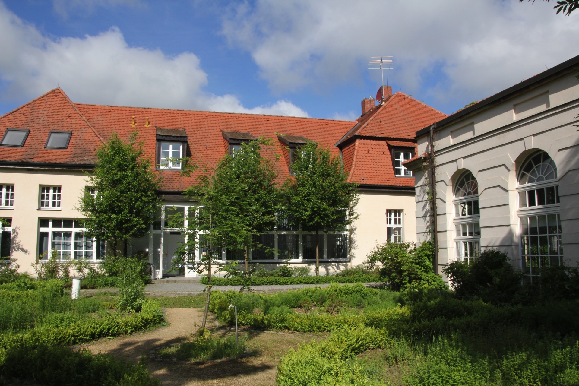 Innenhof am Pförtnerhaus des Hotel Schloss Storkau mit Kräutergarten, rotem Ziegeldach mit Gauben und Bogenfenstern des Palmenhauses