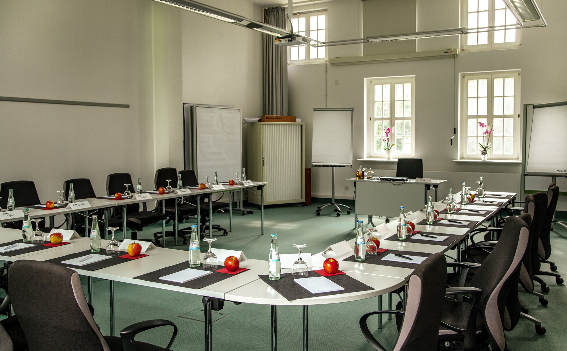 Tagungsraum im Palmenhaus des Hotel Schloss Storkau in U-Form mit Flipcharts und hohen Sprossenfenstern, grüner Teppichboden