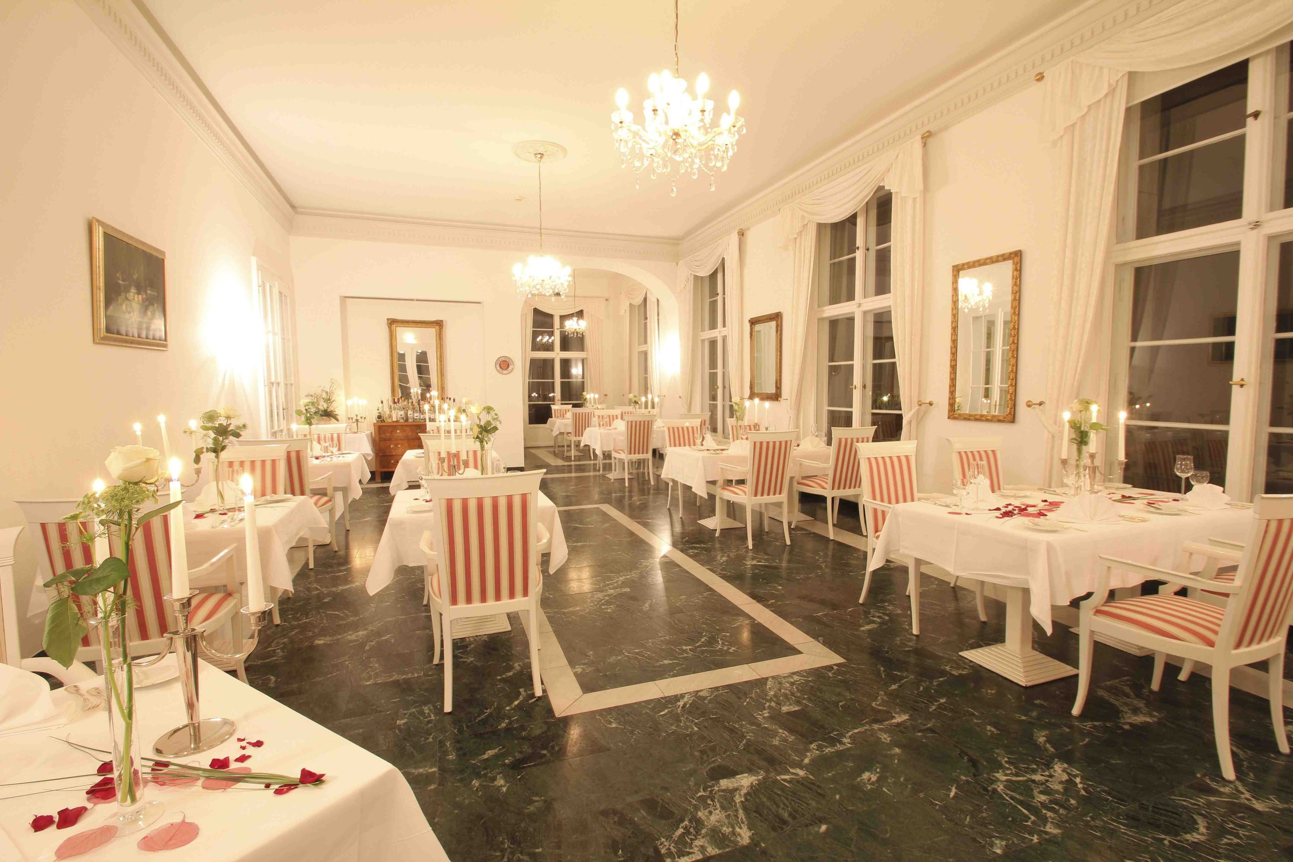 Festlich beleuchteter Speisesaal im Hotel Schloss Storkau mit Kerzen, weißen Rosen und Rosenblättern auf den Tischen