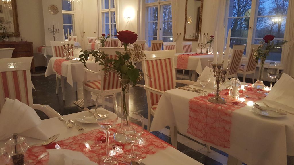 Restaurant im Hotel Schloss Storkau mit roten Tischläufern, Rosen und Kerzenleuchtern in der Abenddämmerung