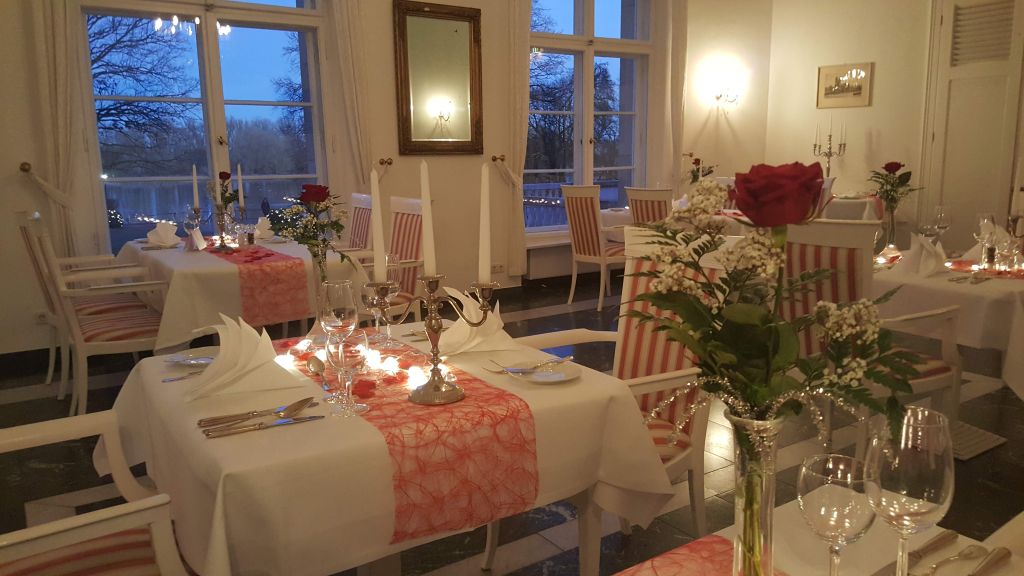 Festlich eingedeckte Tische mit roten Tischläufern, Kerzen und roten Rosen im Restaurant des Hotel Schloss Storkau