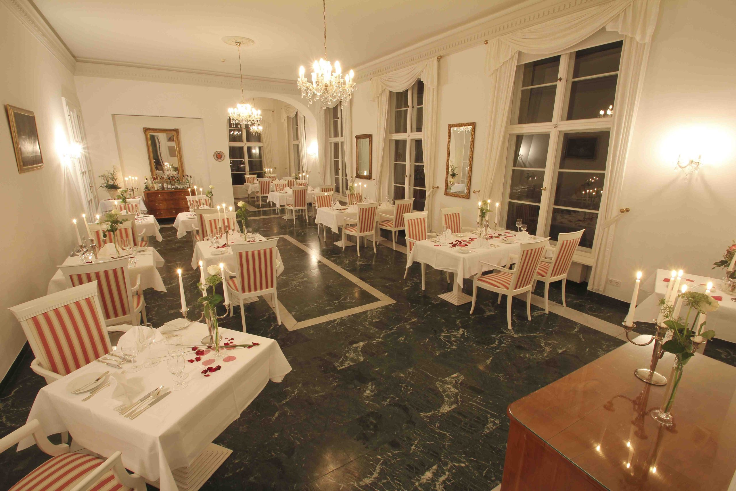 Abendlich beleuchteter Restaurantsaal im Hotel Schloss Storkau mit Kerzenleuchtern, weißen Rosen und Rosenblättern