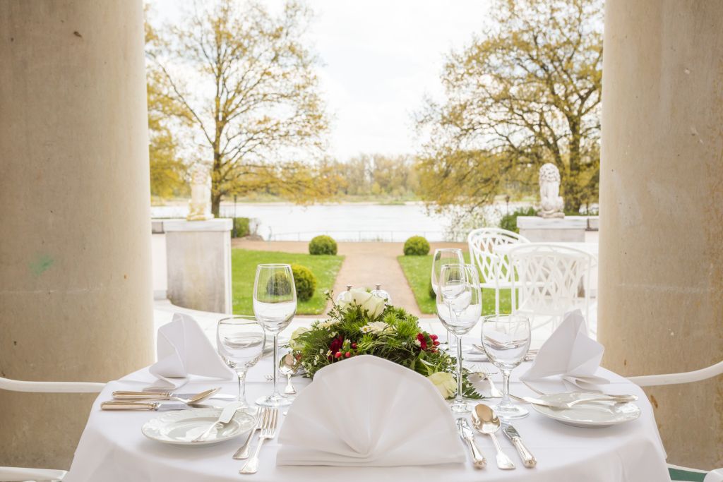 Gedeckter Tisch mit Blumengesteck zwischen den Säulen der Terrasse des Hotel Schloss Storkau mit Blick auf die Elbe