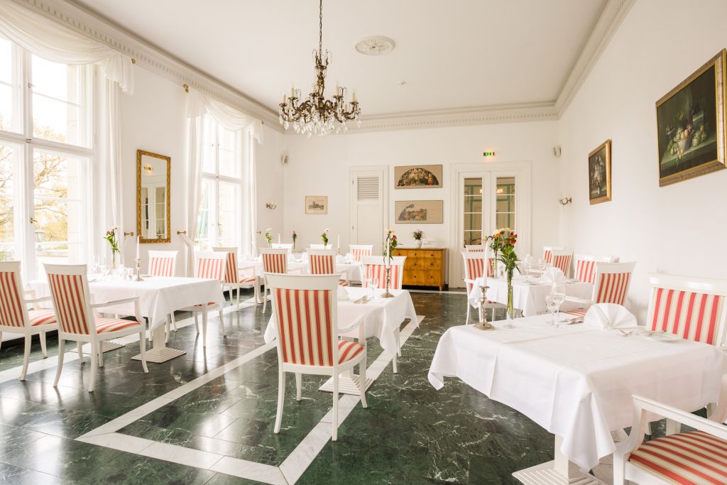 Restaurantsaal im Hotel Schloss Storkau mit Biedermeier-Kommode, Gemälden und weiß gedeckten Tischen