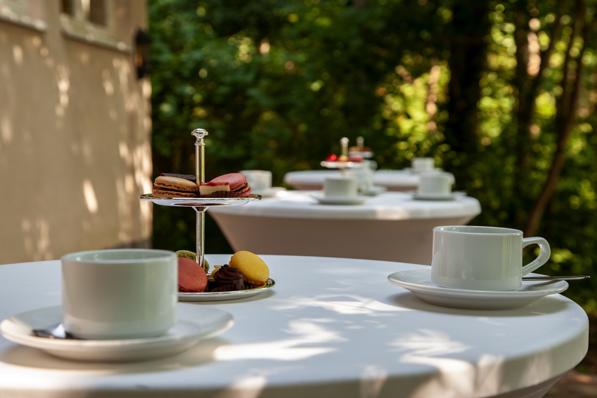 Kaffeepause mit Macarons Kaffee und mehrstöckige Etagere mit Macarons auf weißem Stehtisch im sonnigen Parkbereich von Schloss Storkau.