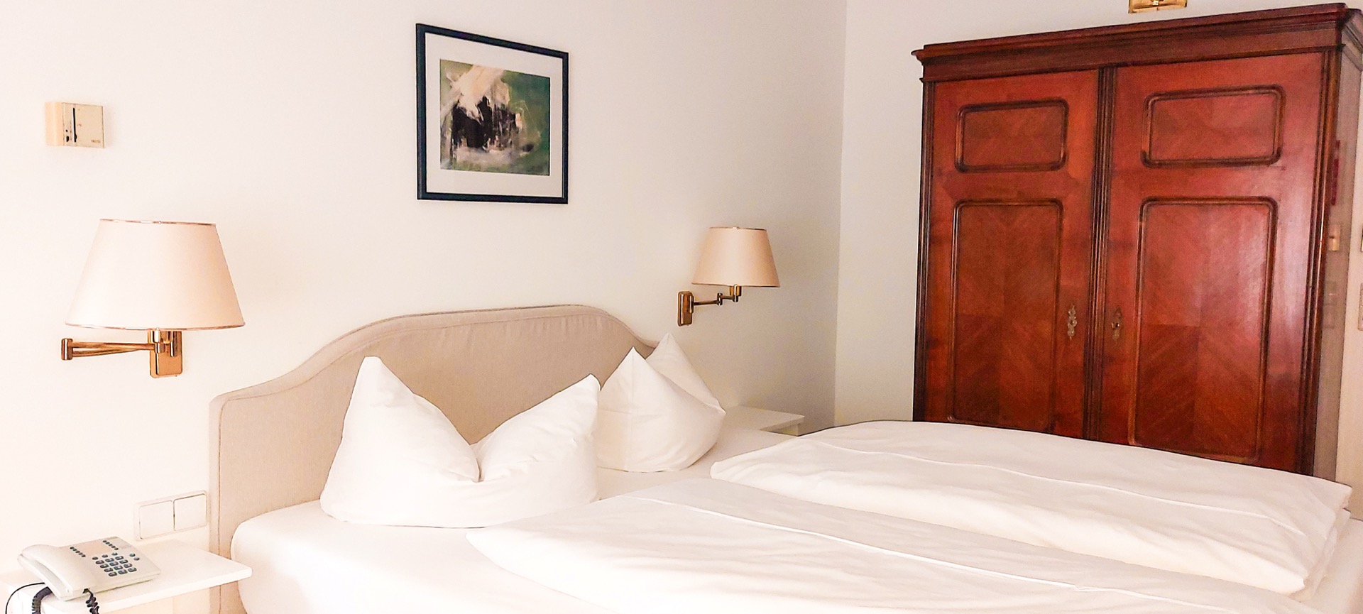 Doppelbett im Comfort-Zimmer des Hotel Schloss Storkau mit antikem Holzschrank und Messing-Wandleuchten