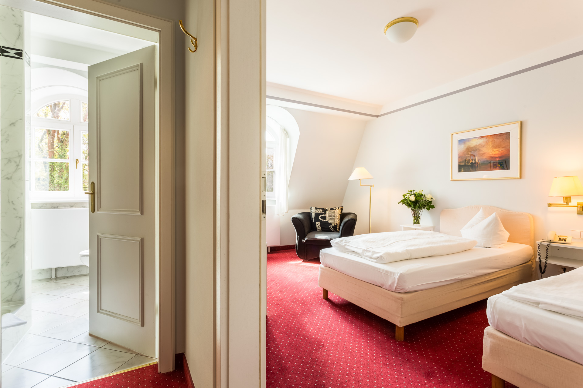 Comfort-Zimmer im Hotel Schloss Storkau mit zwei Einzelbetten, rotem Teppich und Blick in das geflieste Badezimmer