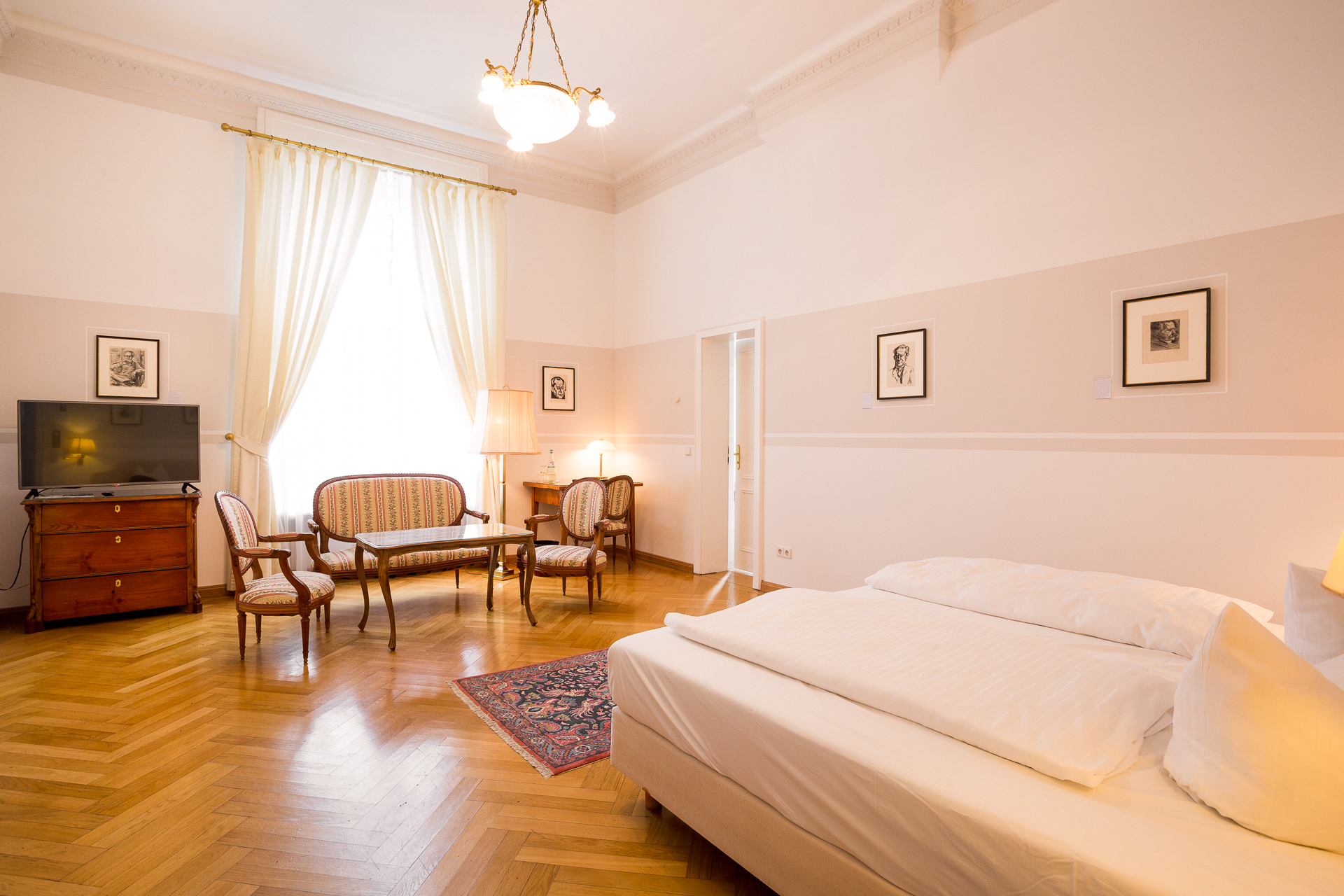 Deluxe-Zimmer im Hotel Schloss Storkau mit gestreifter Polstergarnitur, Fernseher auf antiker Kommode und Doppelbett