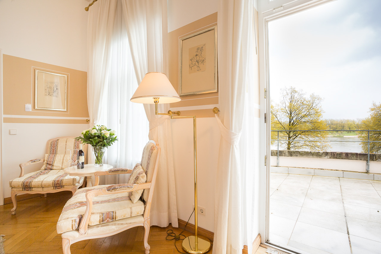 Sitzecke eines Deluxe-Zimmers im Hotel Schloss Storkau mit zwei gestreiften Sesseln und geöffneter Tür zur Terrasse mit Blick auf die Elbe