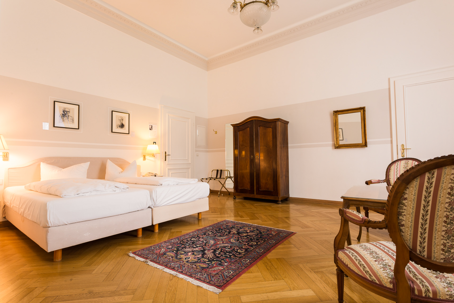 Schlafbereich eines Deluxe-Zimmers im Hotel Schloss Storkau mit Doppelbett, antikem Holzschrank und Orientteppich auf Fischgrätparkett