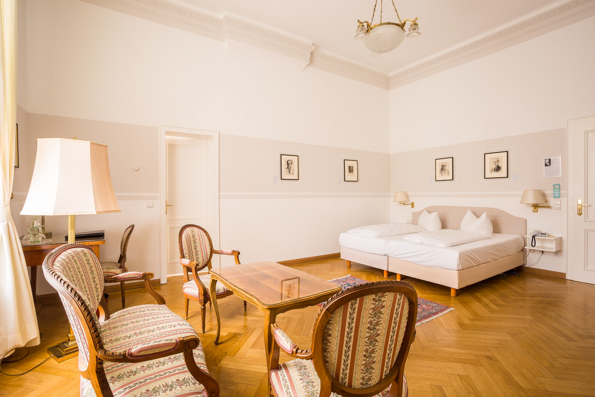 Deluxe-Zimmer im Hotel Schloss Storkau mit hoher Stuckdecke, Kronleuchter, Sitzgruppe und Doppelbett auf Fischgrätparkett