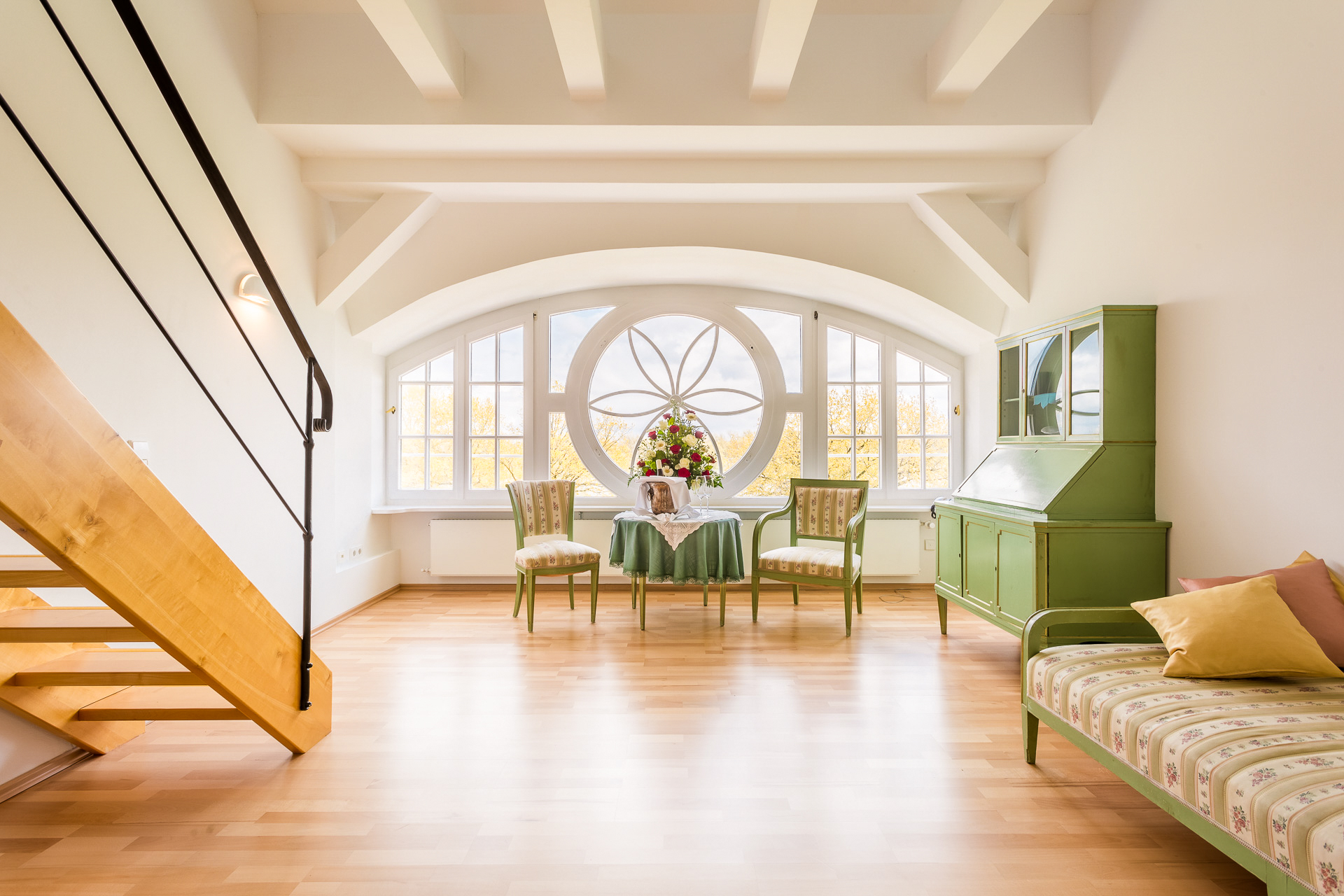 Wohnbereich einer Deluxe-Maisonette im Hotel Schloss Storkau mit Ornament-Rundfenster, grünem Sekretär und Tagesbett