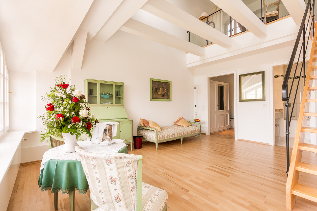 Wohnbereich einer Deluxe-Maisonette im Hotel Schloss Storkau mit Tagesbett, grünem Sekretär und Treppe zur Schlafgalerie