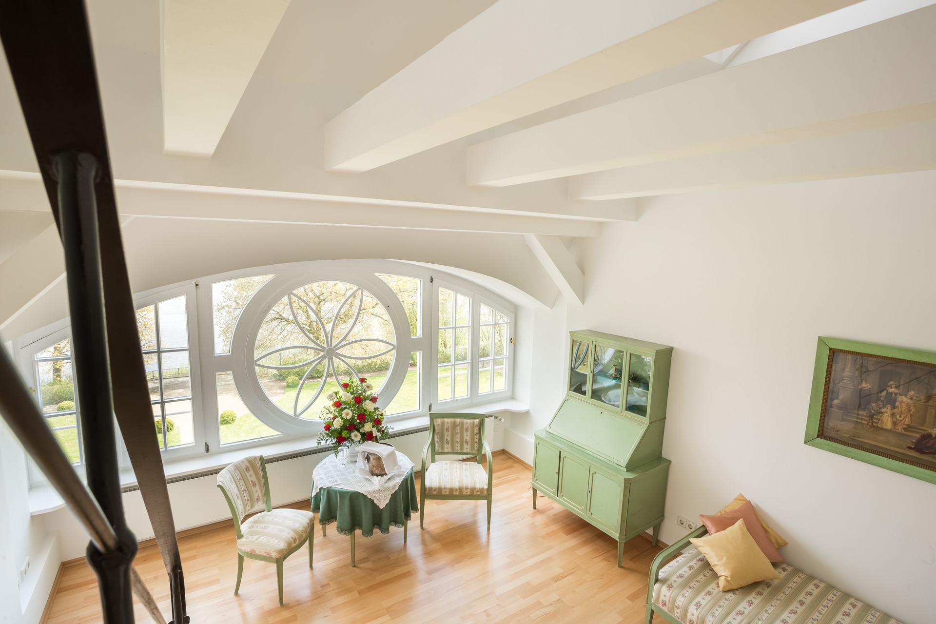 Blick von der Galerie in den Wohnbereich einer Deluxe-Maisonette im Hotel Schloss Storkau mit Ornament-Rundfenster und Parkblick