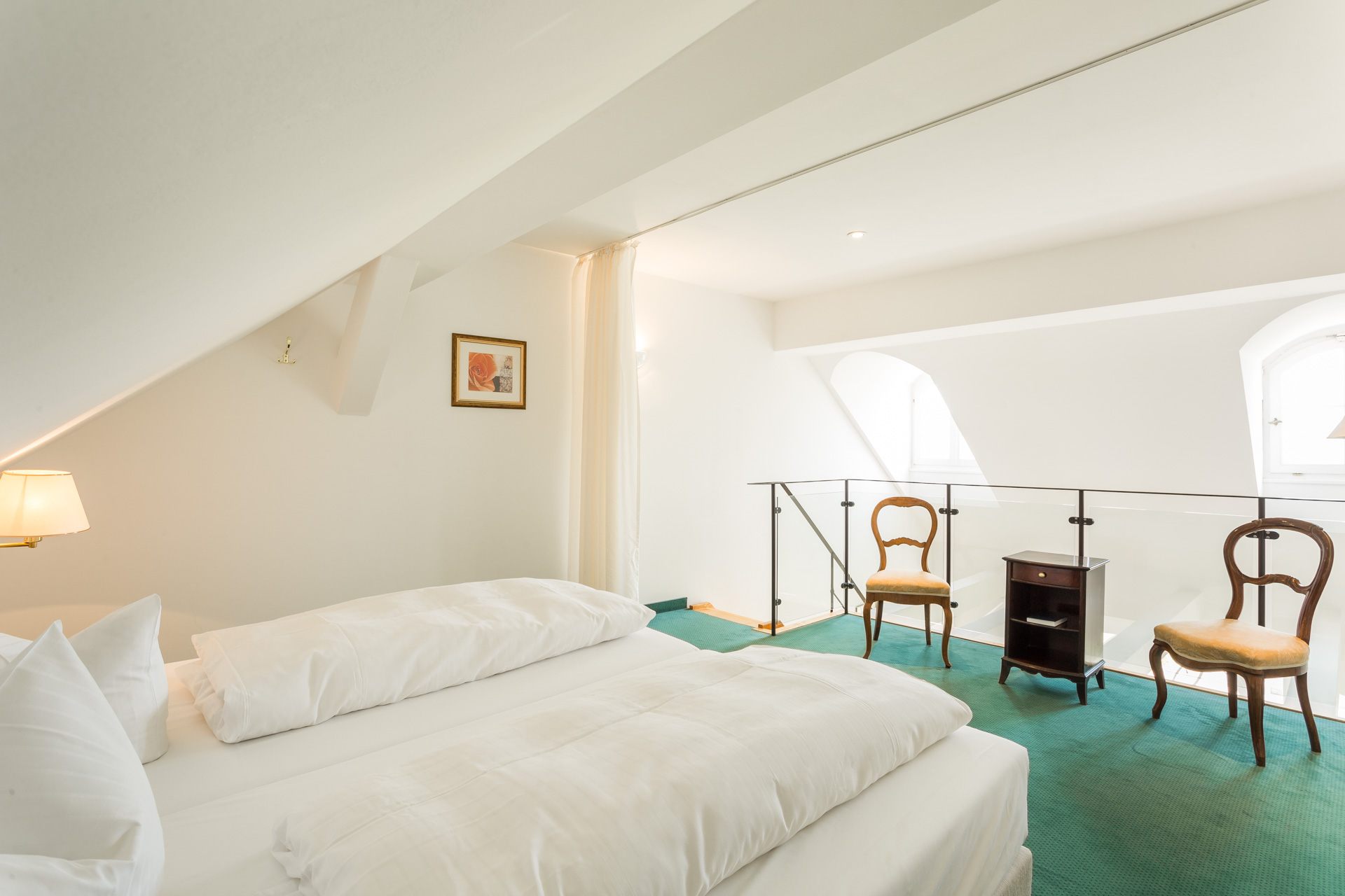 Schlafgalerie einer Deluxe-Maisonette im Hotel Schloss Storkau mit Doppelbett, grünem Teppich und Glasbrüstung