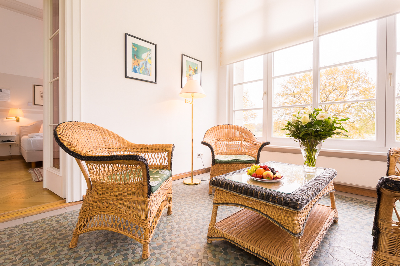 Sitzecke mit Korbmöbeln in einem Deluxe-Zimmer im Hotel Schloss Storkau, auf dem Glastisch ein Obstteller und ein Blumenstrauß