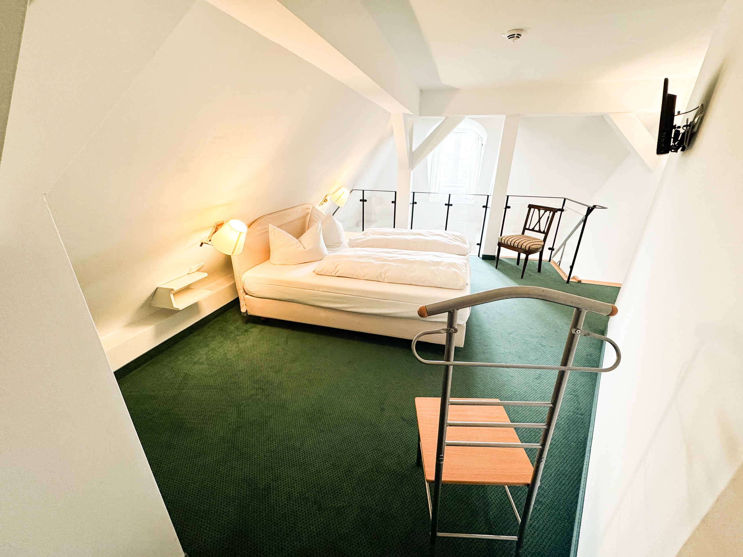 Schlafgalerie einer Deluxe-Maisonette im Hotel Schloss Storkau mit Doppelbett, grünem Teppichboden und Glasbrüstung über dem Wohnbereich