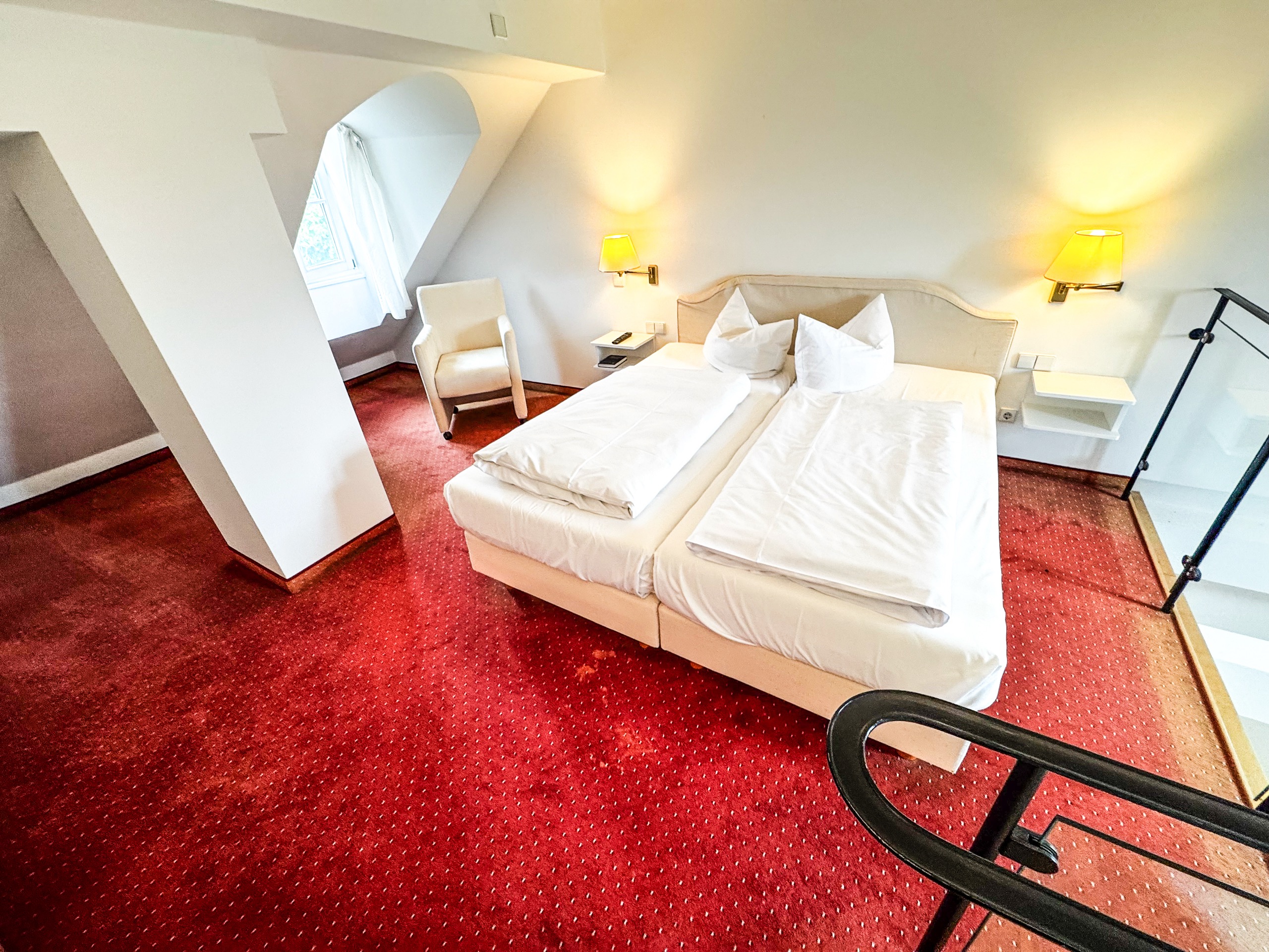 Schlafbereich auf der Galerie einer Maisonette im Hotel Schloss Storkau mit Doppelbett, weißer Bettwäsche und rotem Teppichboden