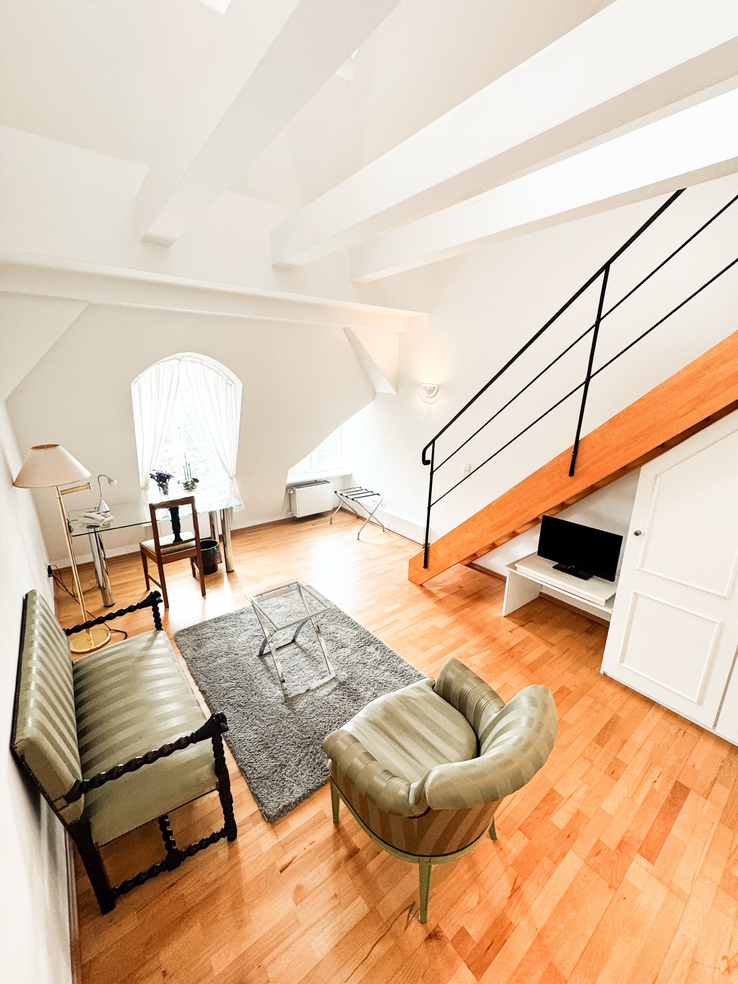 Wohnbereich einer Maisonette im Hotel Schloss Storkau mit grüner Sitzbank, Sessel, grauem Teppich und Treppe zur Galerie