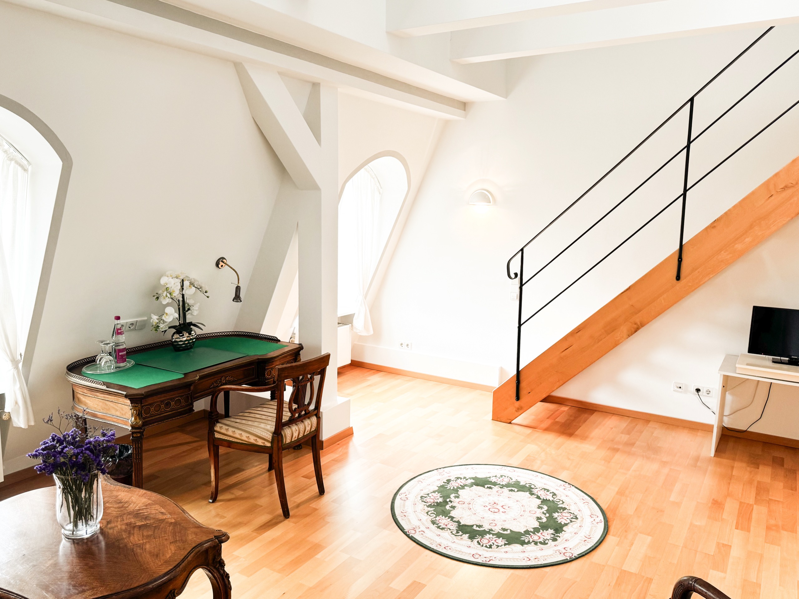 Antiker Schreibtisch mit grüner Schreibauflage und Orchidee in einer Maisonette im Hotel Schloss Storkau, dahinter die Treppe zur Galerie