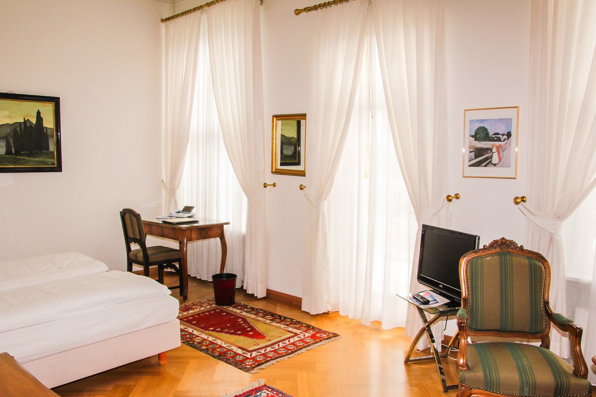 Premium-Zimmer im Hotel Schloss Storkau mit Bett, antikem Schreibtisch am Fenster, gestreiftem Sessel und Orientteppich auf Parkett