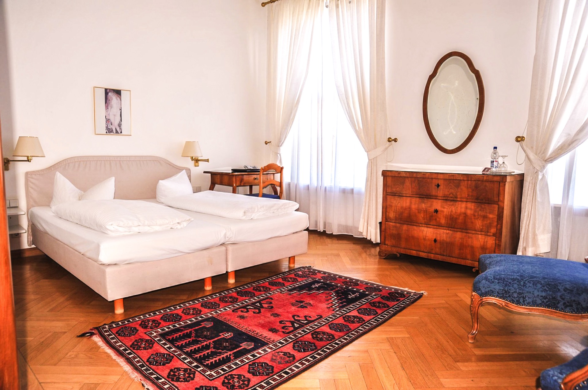 Helles Premium-Zimmer im Hotel Schloss Storkau mit Doppelbett, Biedermeier-Kommode, ovalem Spiegel und rotem Orientteppich