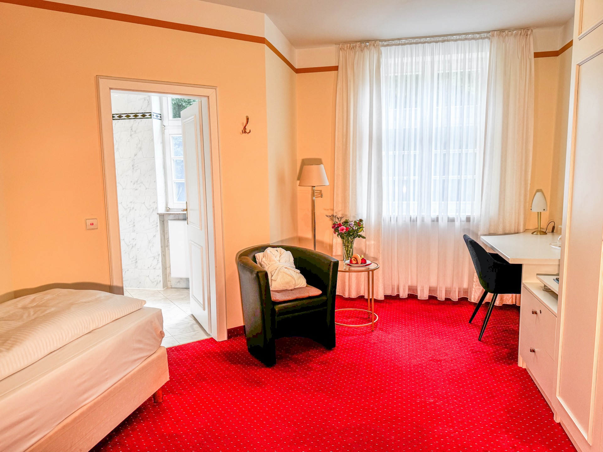 Standard-Zimmer im Hotel Schloss Storkau mit Einzelbett, Ledersessel mit Bademantel und Blick ins marmorgeflieste Badezimmer
