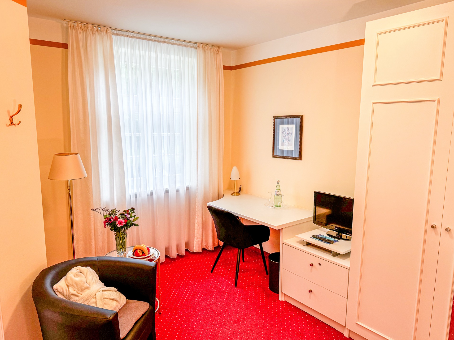Standard-Zimmer im Hotel Schloss Storkau mit Ledersessel, Blumenstrauß, Schreibtisch mit Fernseher und weißem Kleiderschrank