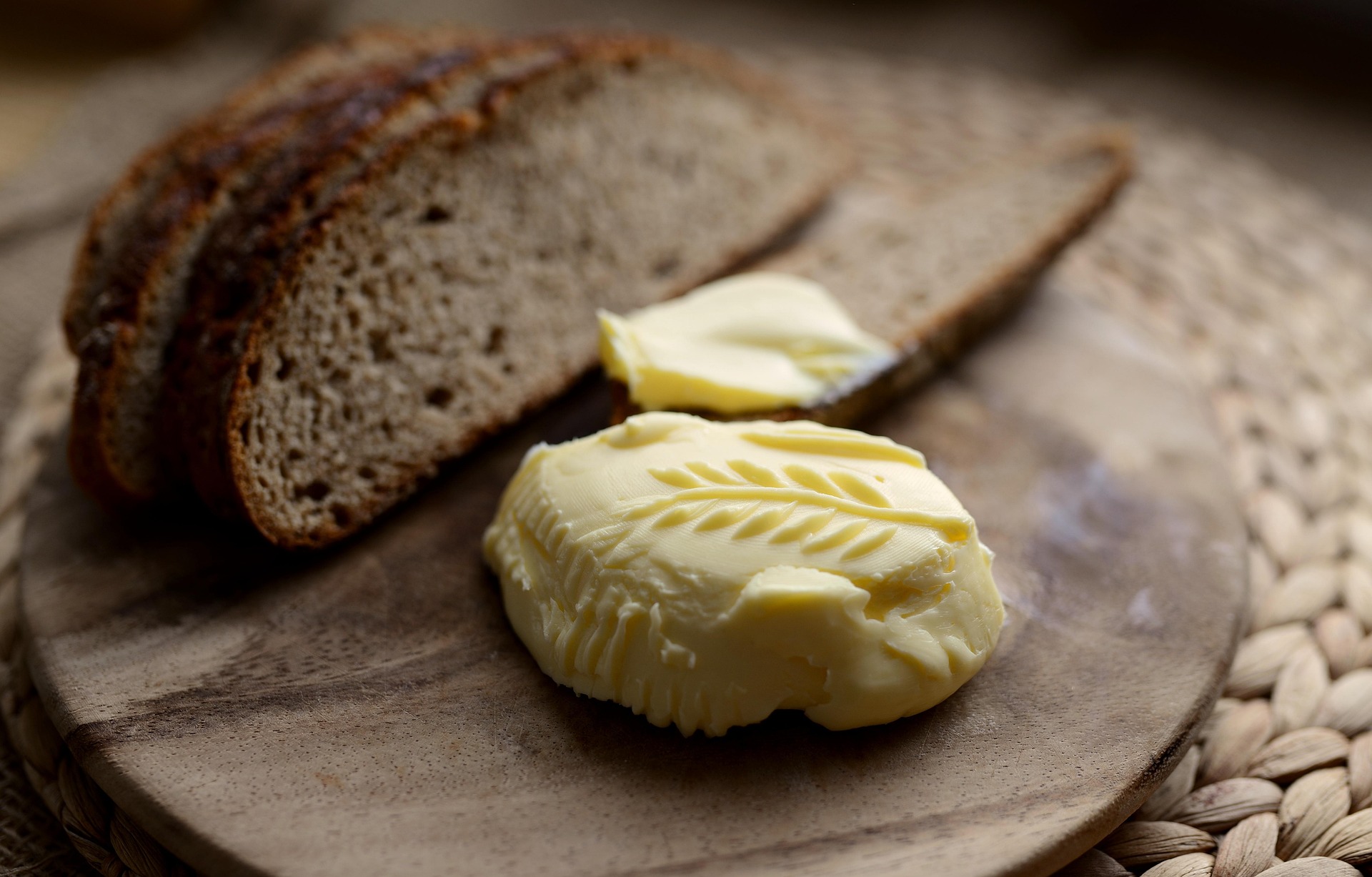 Butter mit Ährenrelief Butter mit geprägtem Ährenmuster auf einem Holzbrett, dahinter Scheiben dunkles Brot und ein Messer mit Butter