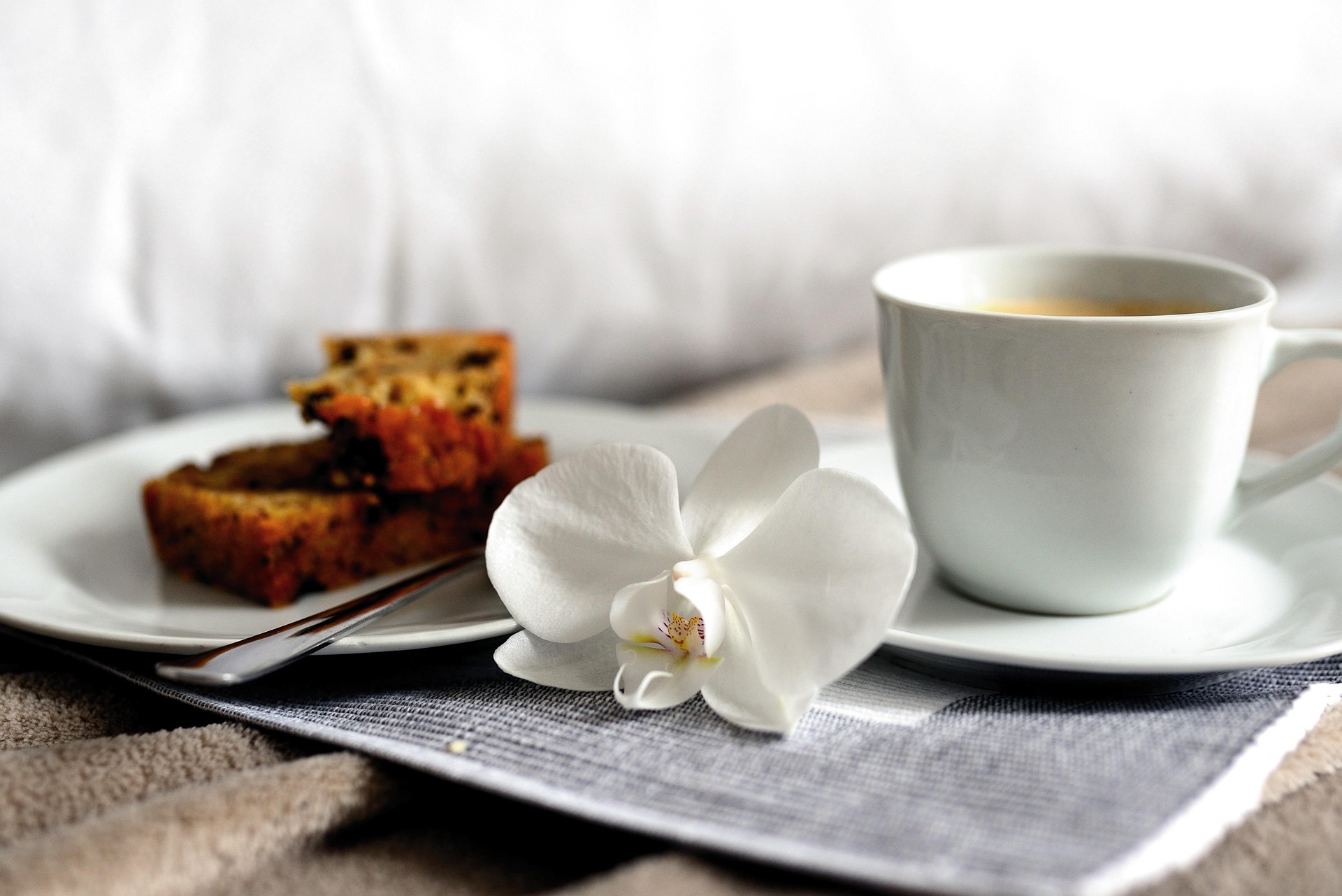 Frühstück ans Bett Frühstückstablett im Bett mit Kaffeetasse, Kuchenstücken und weißer Orchideenblüte