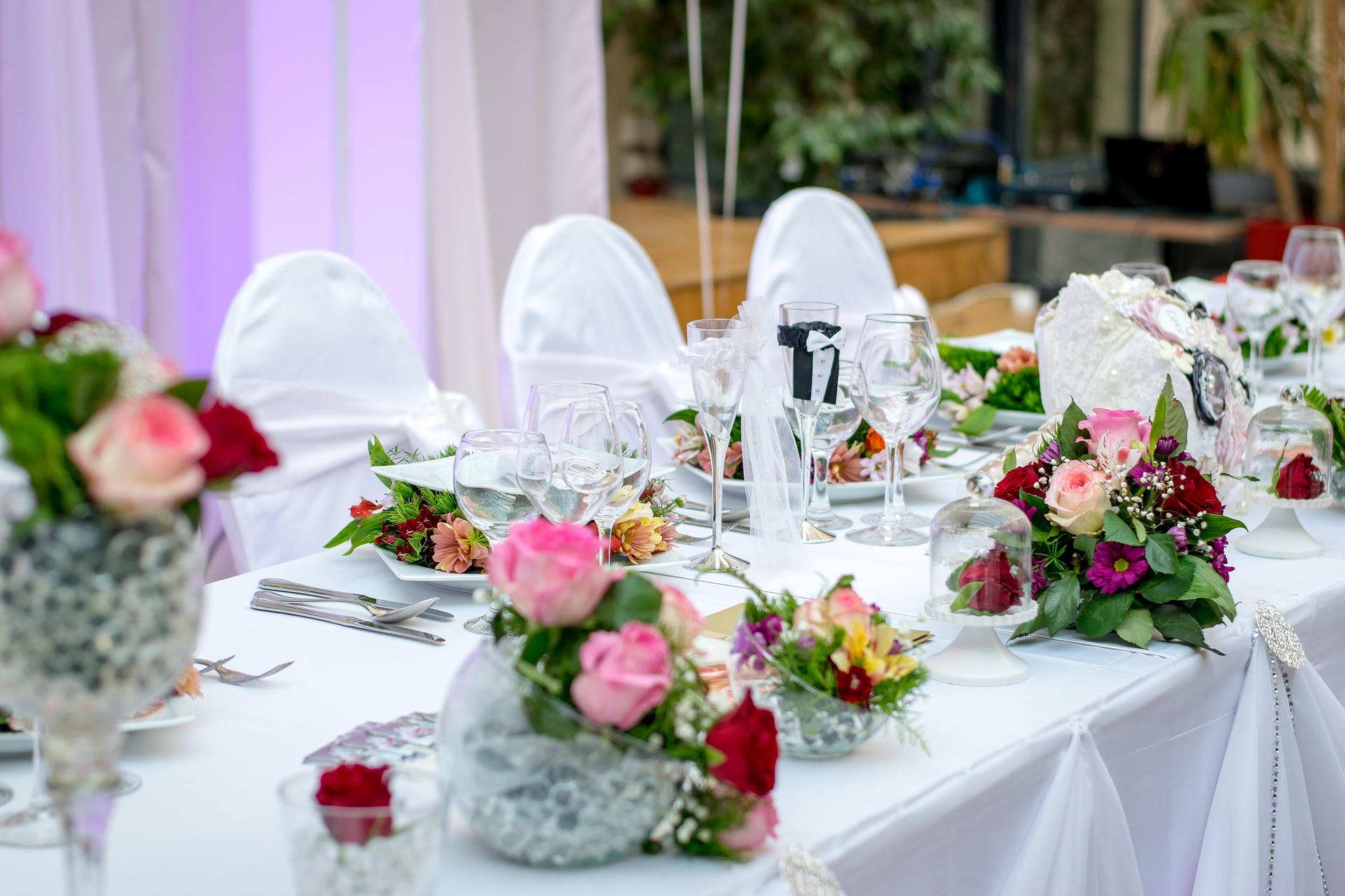 Hochzeitstafel mit Blumendekoration Festlich gedeckte Hochzeitstafel mit weißen Stuhlhussen, Rosengestecken und dekorierten Sektgläsern