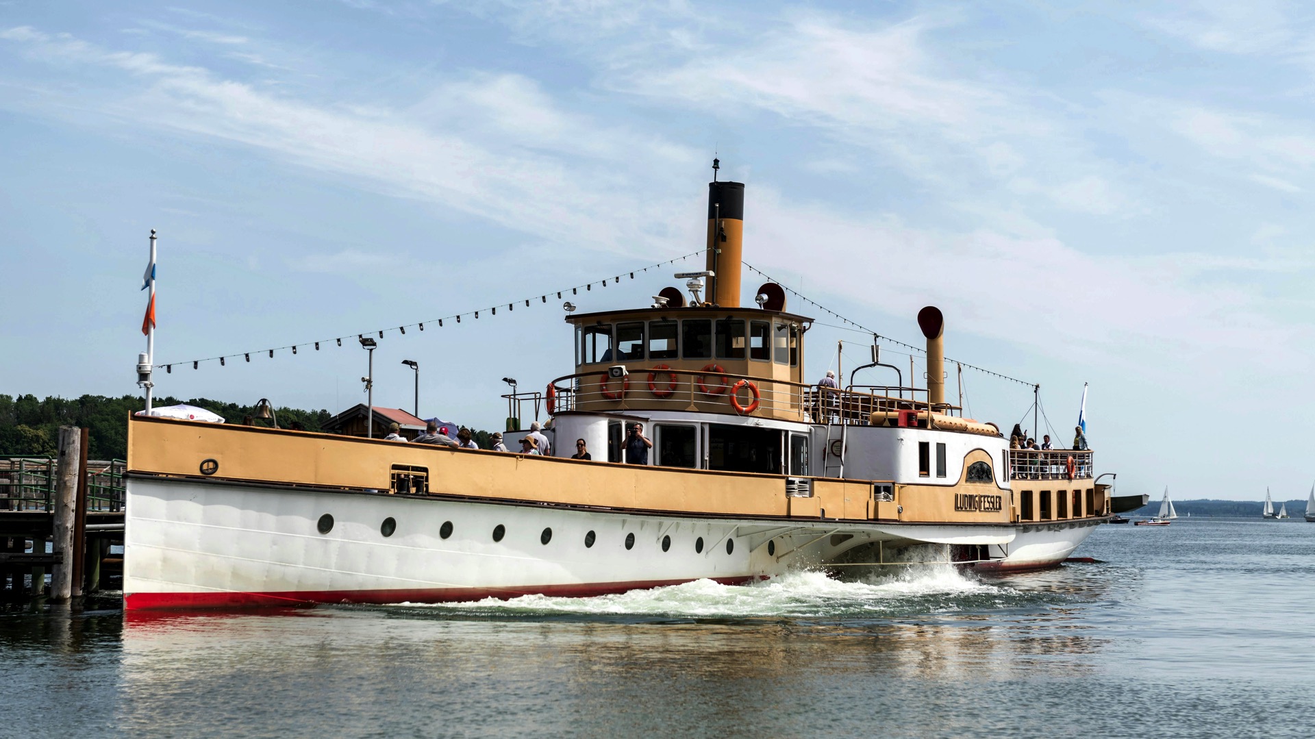 Historischer Raddampfer mit Passagieren an Deck legt an einem hölzernen Bootssteg an